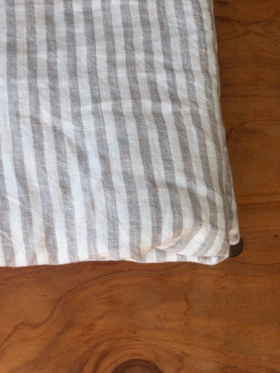 The corner of a neatly folded grey and white striped coloured French flax linen duvet cover on a wooden surface