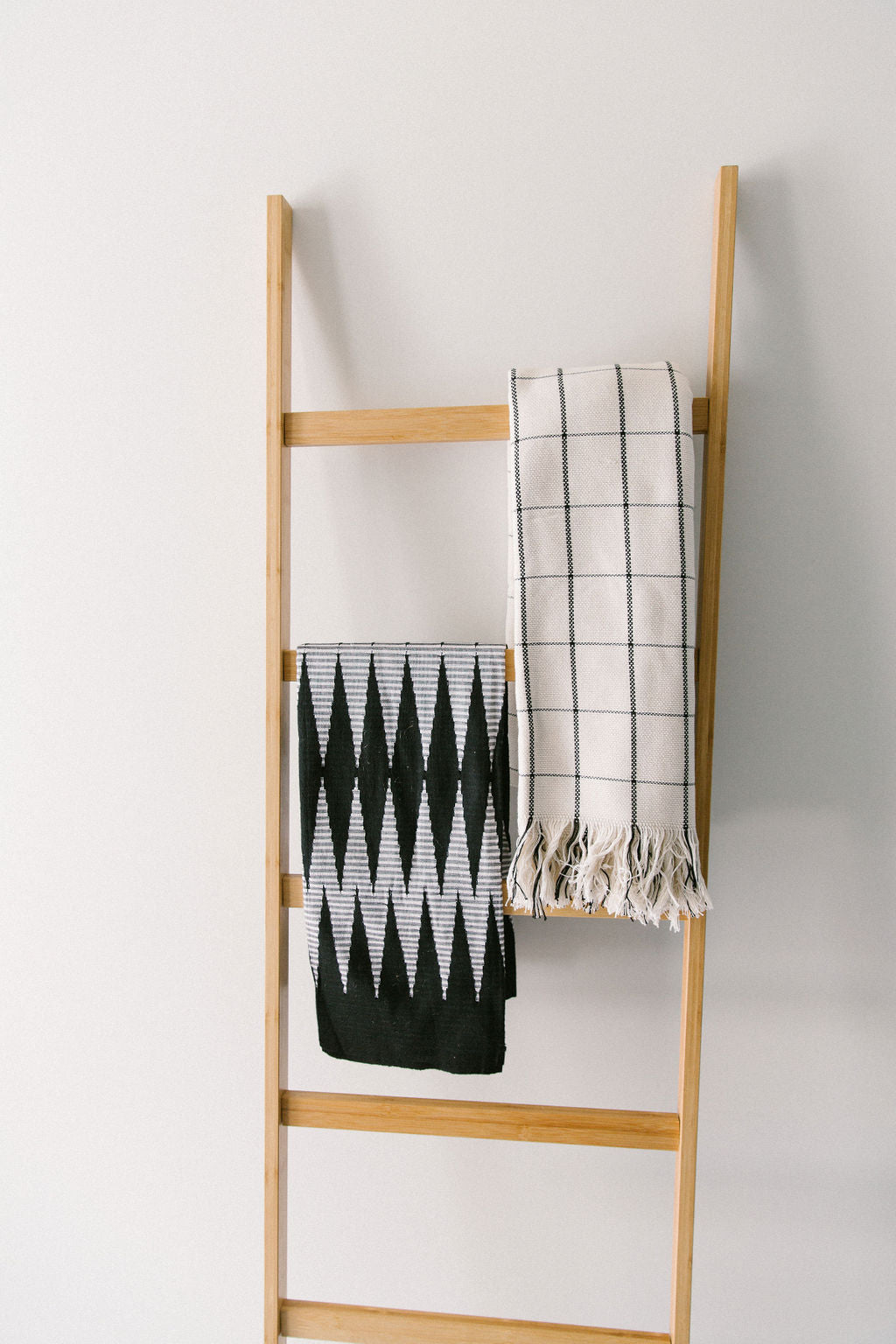 Wooden ladder with two handwoven cotton throw blankets on a white background.