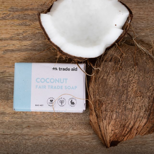 Bar of coconut Fair Trade soap from Trade Aid on a wooden surface with a half-coconut.