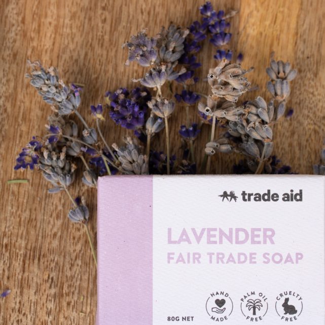 Lavender soap bar with 'Trade Aid' branding on a wooden surface with lavender flowers.