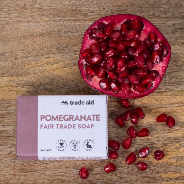 Pomegranate Fair Trade soap from Trade Aid on a wooden surface with pomegranate seeds.