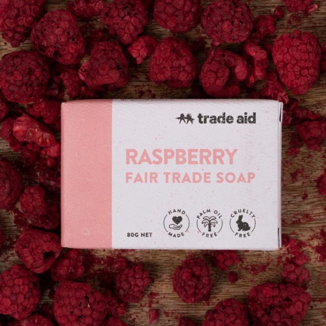 Trade Aid raspberry fair trade soap bar surrounded by raspberries on a wooden surface