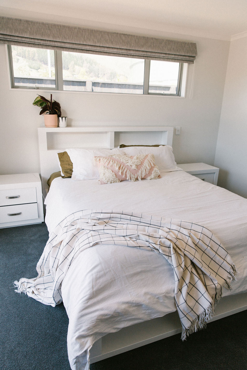 Neatly made bed with white bedding and white and black plaid blanket in a bedroom setting.