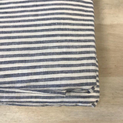The corner of a neatly folded French linen duvet cover, with navy and off-white stripes on a wooden surface