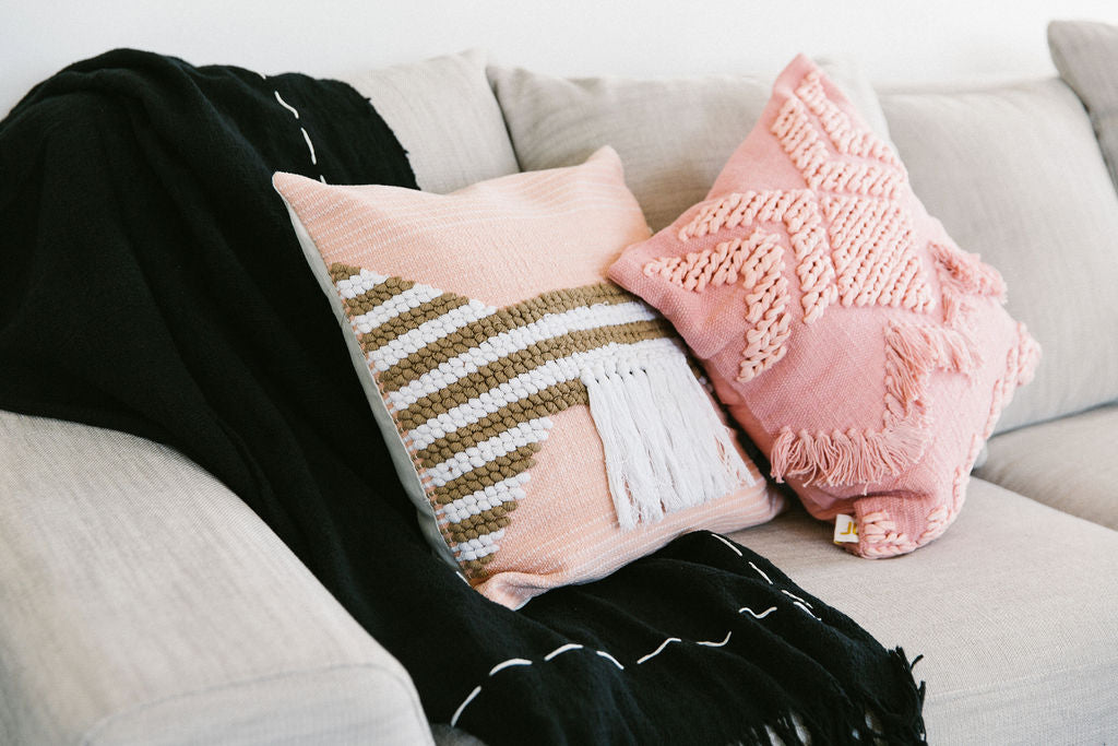 Two decorative pillows on a couch with a black blanket draped over them.
