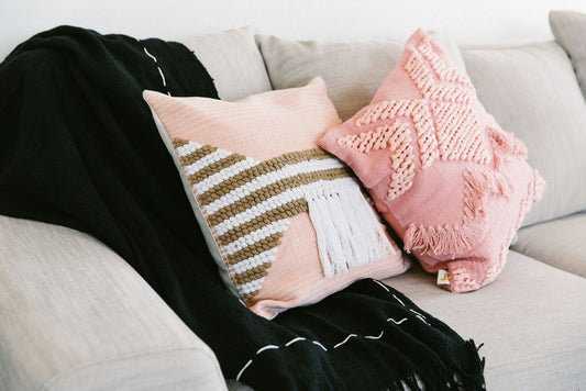 Two decorative pillows on a couch with a black blanket draped over them.