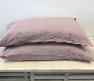 Two blush pink coloured French flax pillows on a light wood surface with a white background.