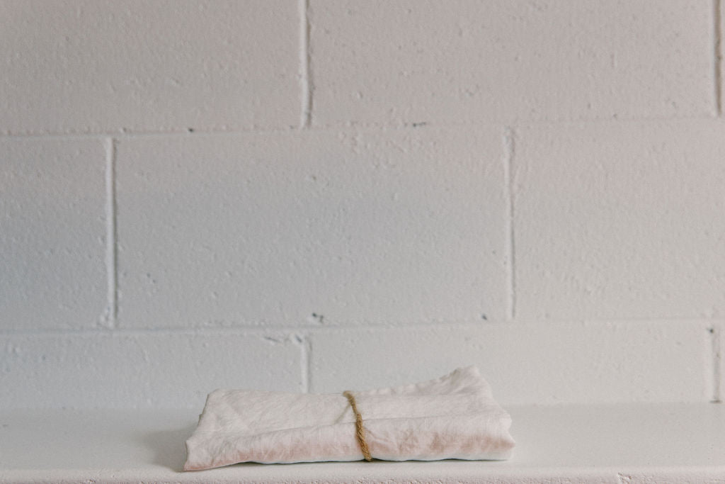 A French linen duvet cover in a crisp white colour on a white brick background, neatly folded and tied with brown twine