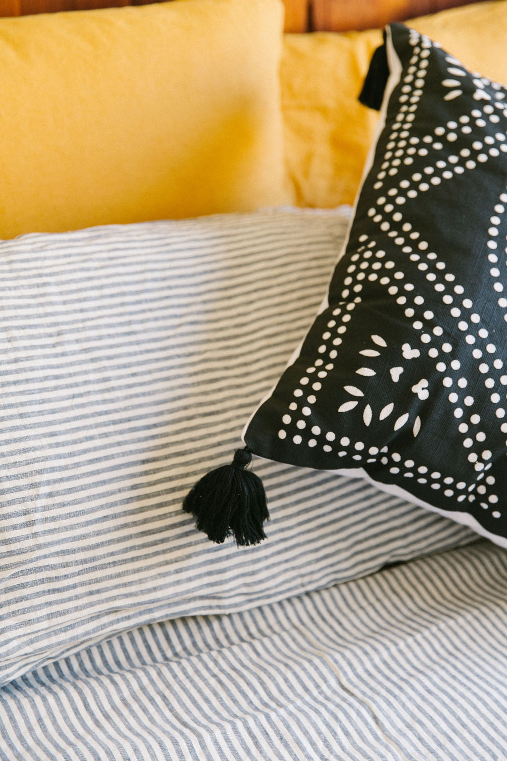 Black pillow with white patterns and tassels on a striped french linen background. Close up view of kim soo dot print cushion cover detail