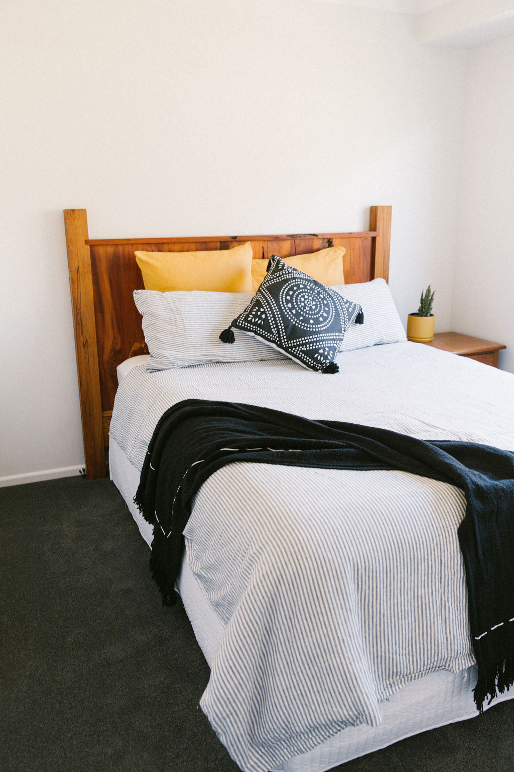 Bed with wooden headboard, white bedding, and decorative Kim Soo cushions in a bedroom setting.