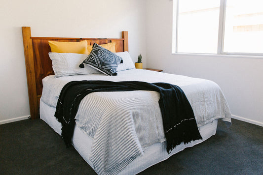 Bedroom with a wooden bed frame, navy and off white French linen duvet, a black throw and decorative pillows.
