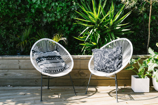 Two outdoor chairs with patterned kim soo printed cushions on a wooden deck with plants in the background