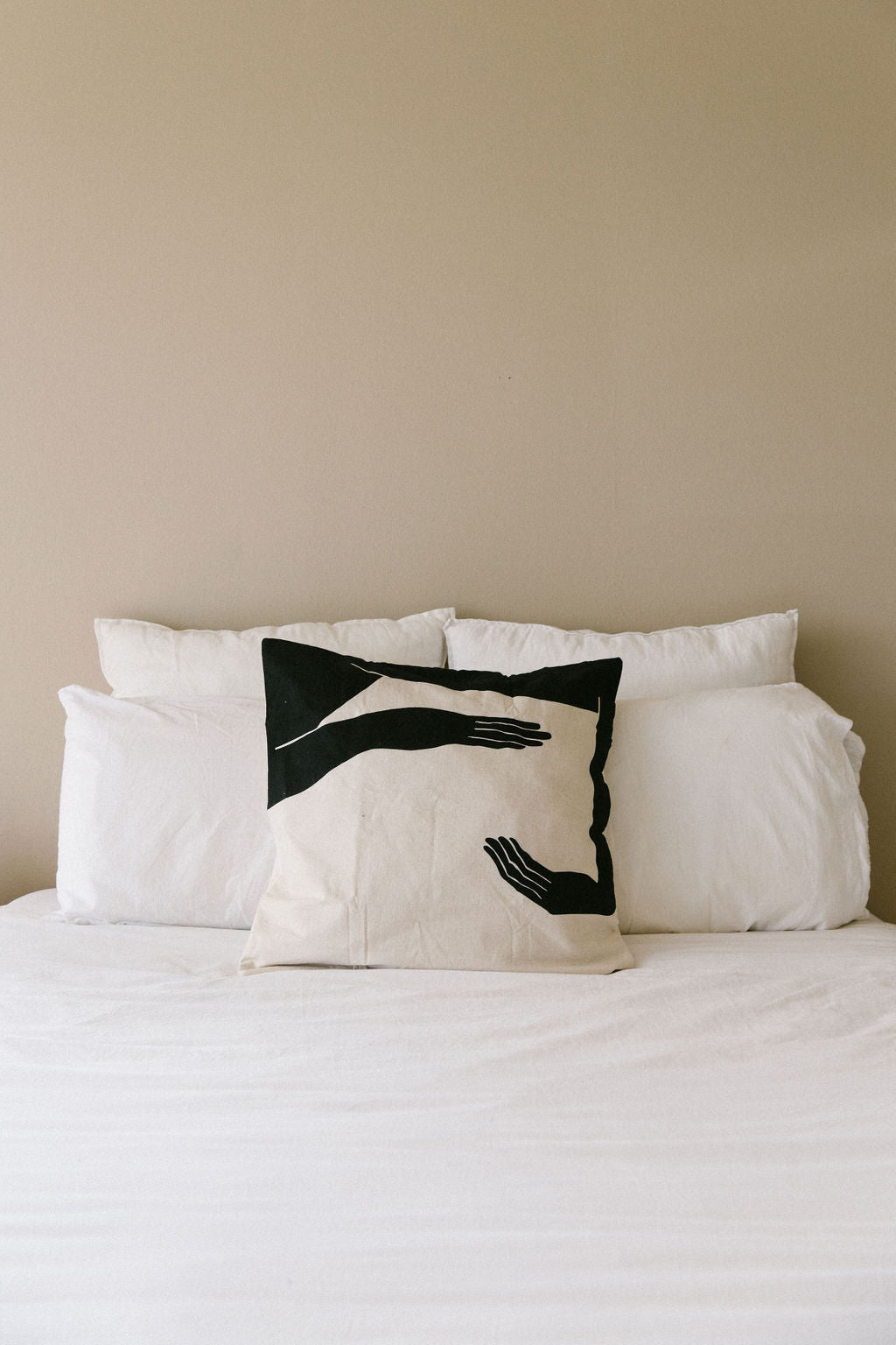 Decorative kim soo Linen rayon pillow with black hand design on a bed against a beige wall
