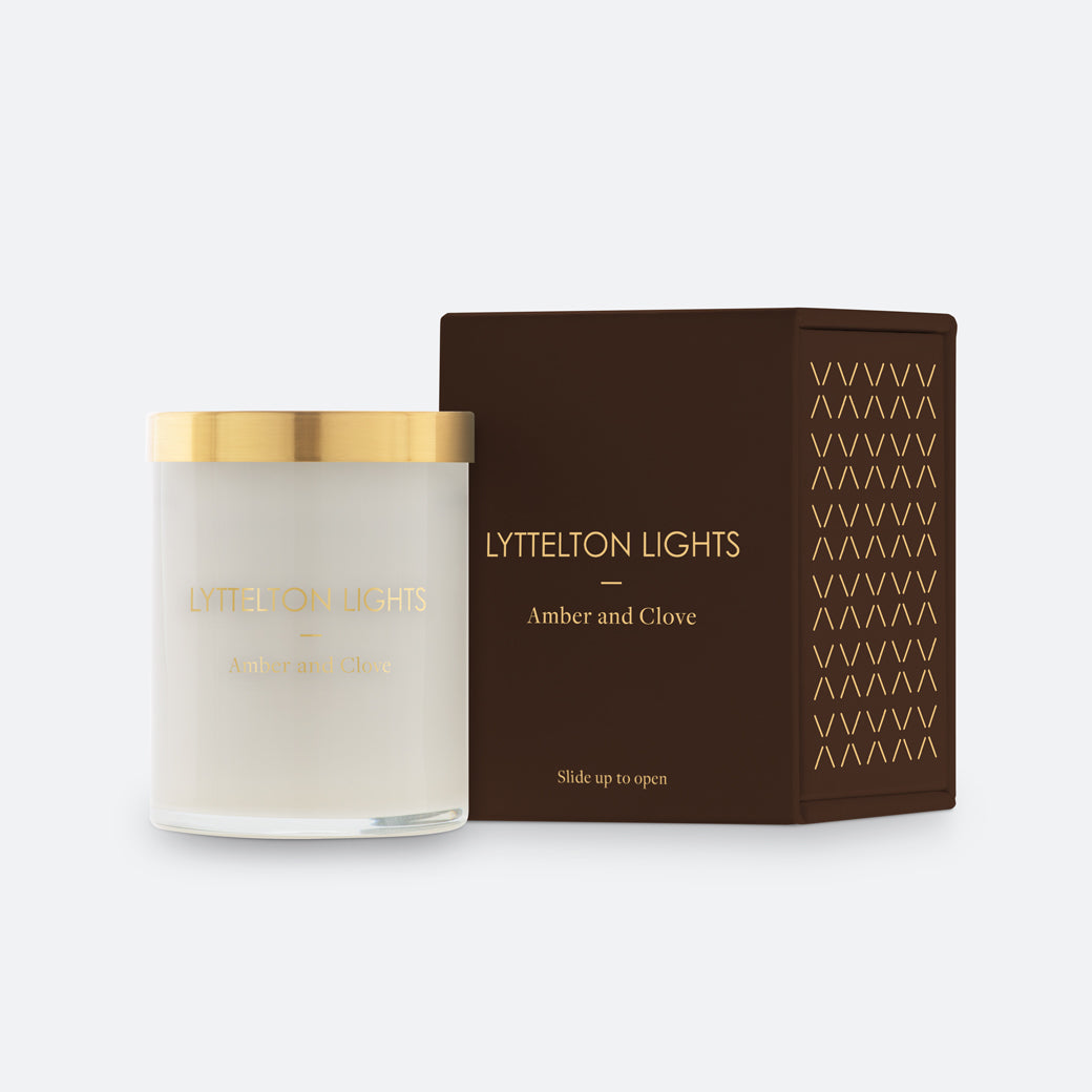 Lyttelton Lights Amber and Clove candle with gold lid and matching brown packaging on a white background