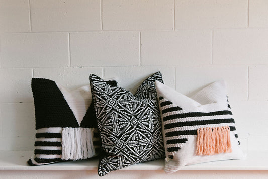 Three decorative pillows with black, white, and pink patterns on a white brick wall background. By Kim Soo