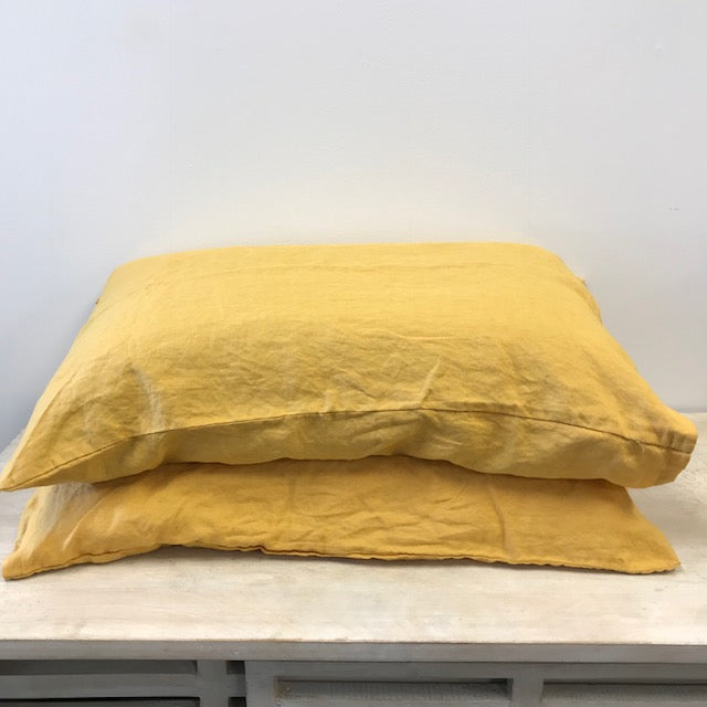 Two mustard coloured French flax pillows on a light wood surface with a white background.