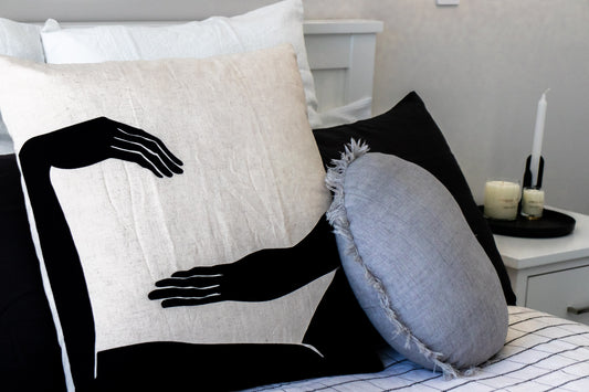 Decorative kim soo pillow with black silhouette of a persons hands on a bed