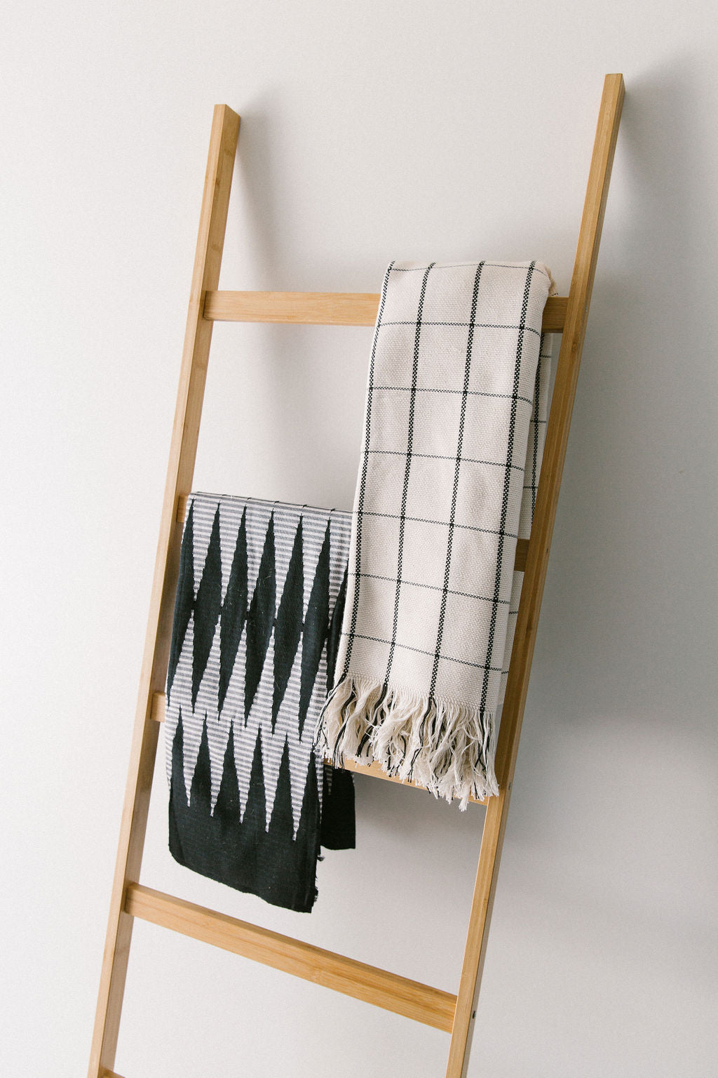 Wooden ladder with two kim soo blankets draped over it against a white wall
