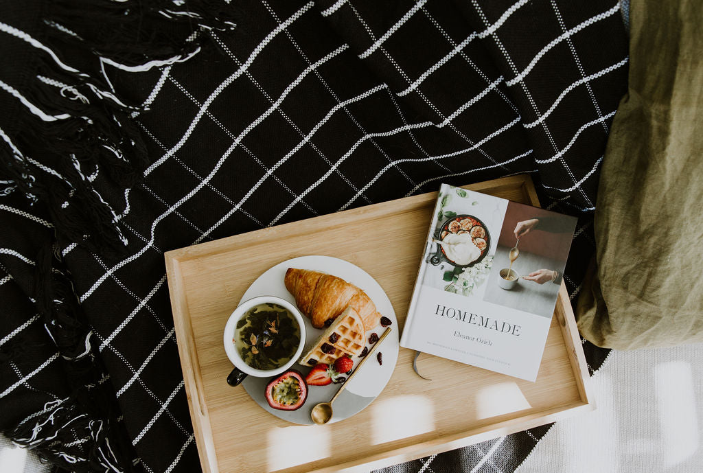 Wooden tray with a plate of food and a book titled 'Homemade' on a black and white checkered blanket.