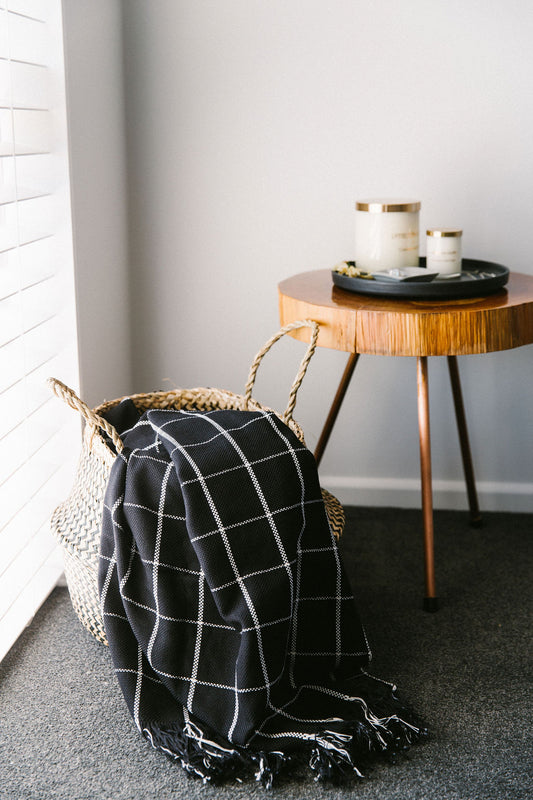 Black checkered blanket draped over a chair next to a wooden side table with candles.