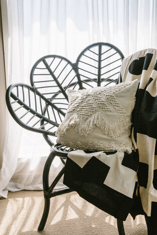 Black wicker chair with a textured pillow and black and white patterned kim soo blanket in a bright room.