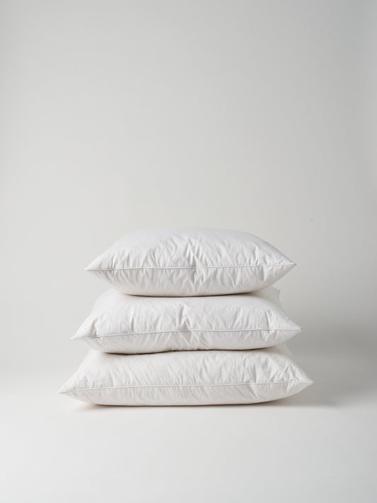 Three white cushion inners of different sizes, stacked on top of eachother, on a white background.